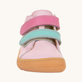 A front on view of the Froddo first step shoes in pink available at Babipur. A soft ankle high natural leather shoe in light pink with 2 velcro straps on the front in dark pink and light blue. Features a light brown rubber grippy sole and a padded ankle support.