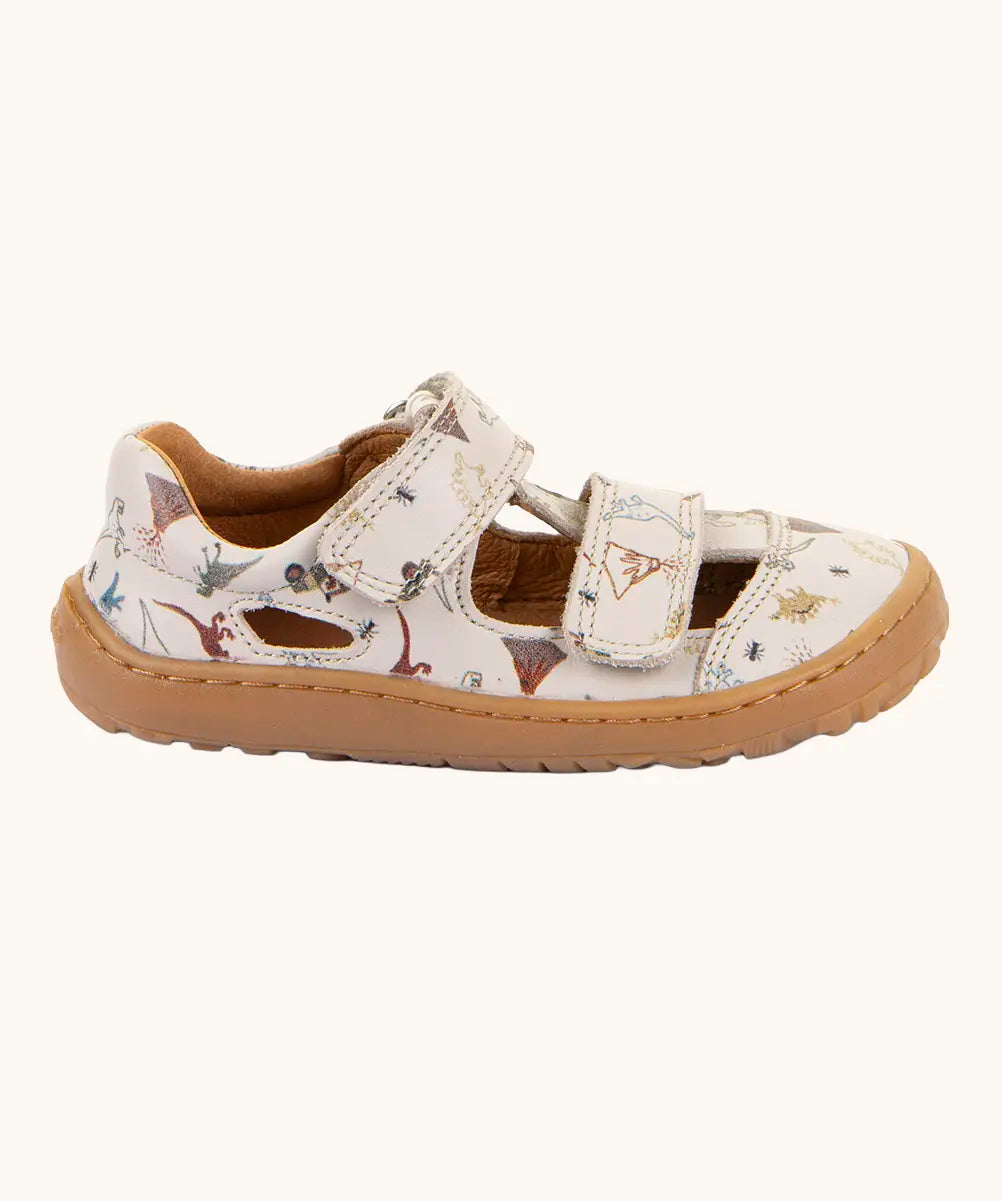 Side of the Froddo barefoot kids sandals in beige with a dinosaur themed outline print.