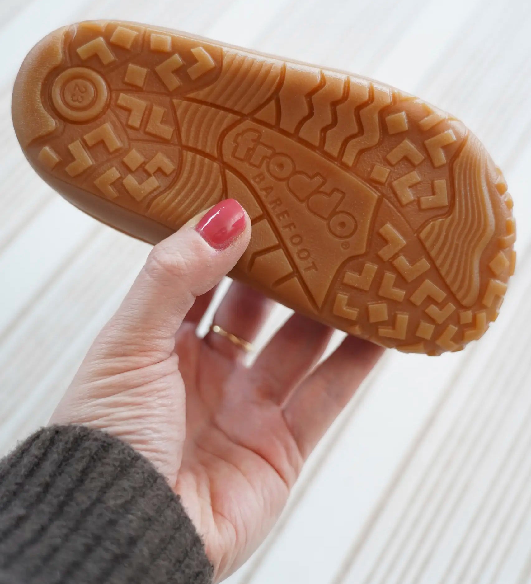Adult hand holding a Froddo barefoot kids shoe showing the tread detail on the rubber sole