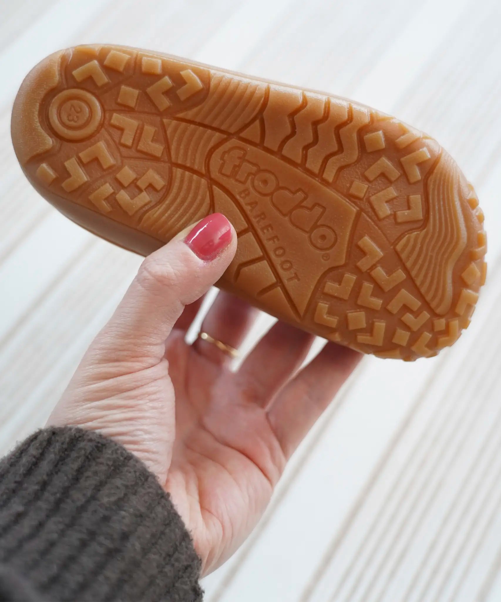 Adult hand holding a Froddo barefoot kids shoe showing the tread detail on the rubber sole