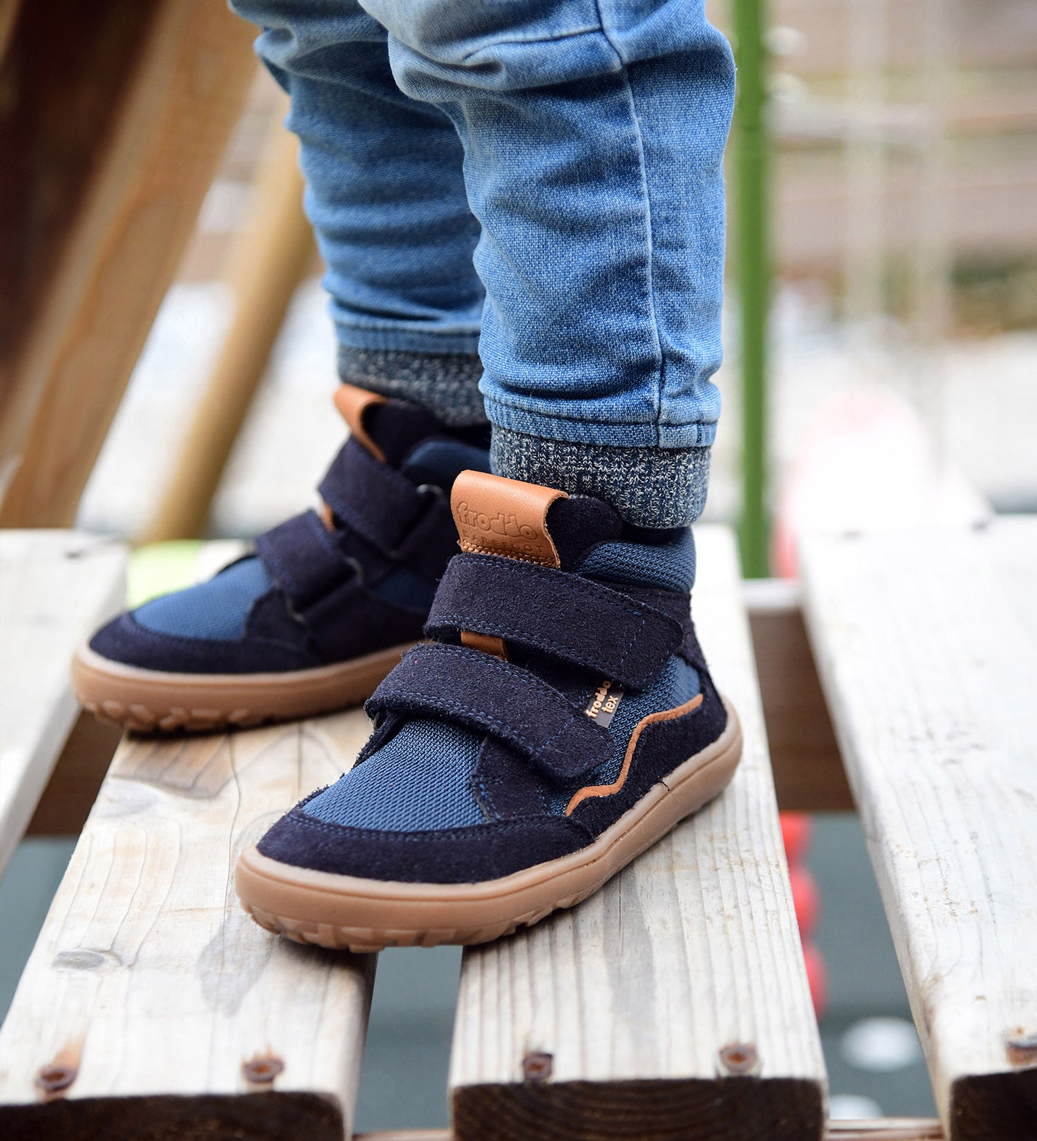 A close up of a child wearing the Froddo barefoot Tex Autumn children's shoe in dark blue available at Babipur. A children's waterproof shoe with a 2 velcro fastener on the front for a secure fit, padded ankle and a brown grippy sole.