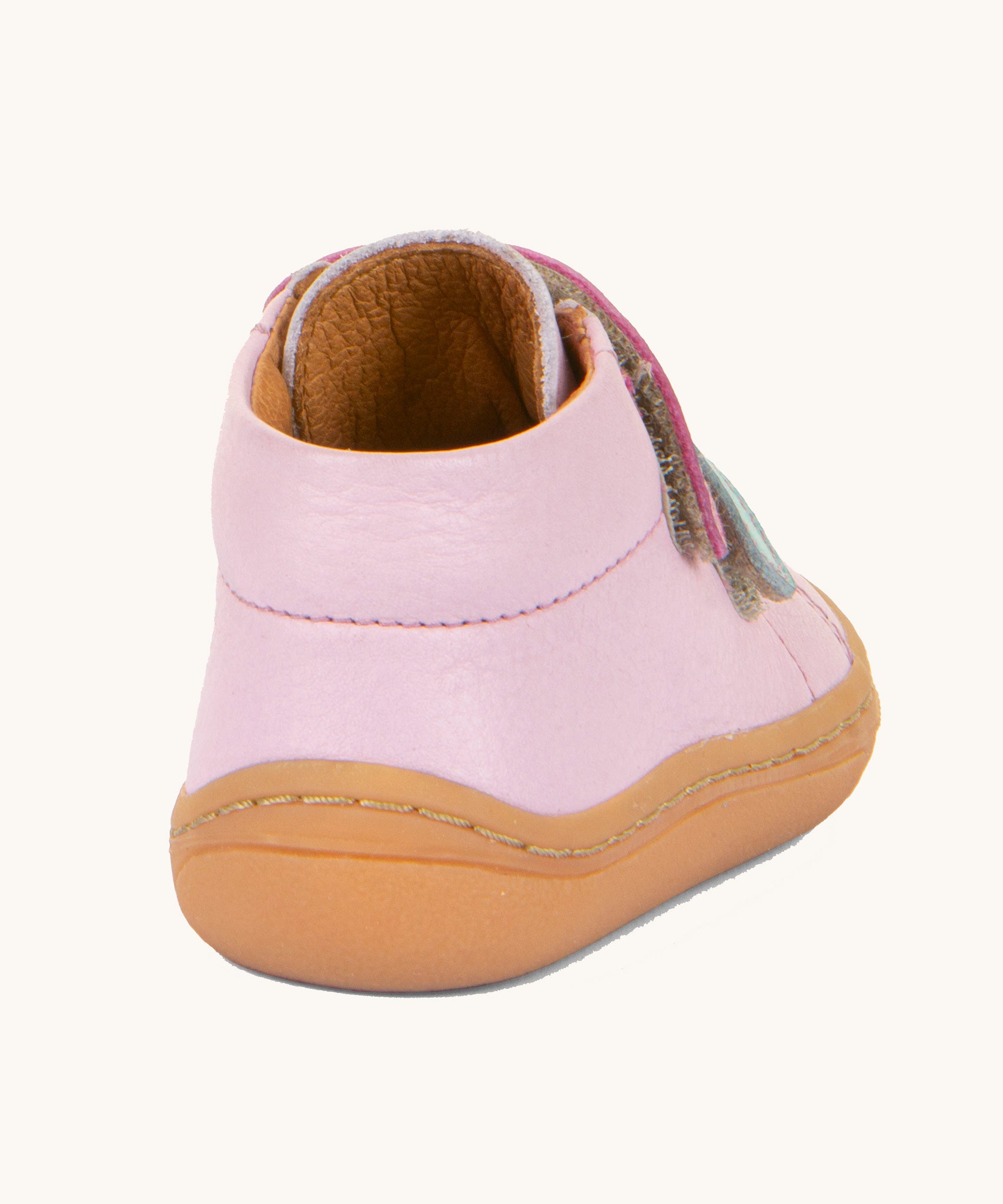 A view of the back of the Froddo first step shoes in pink available at Babipur. A soft ankle high natural leather shoe in light pink with 2 velcro straps on the front in dark pink and light blue. Features a light brown rubber grippy sole and a padded ankle support.