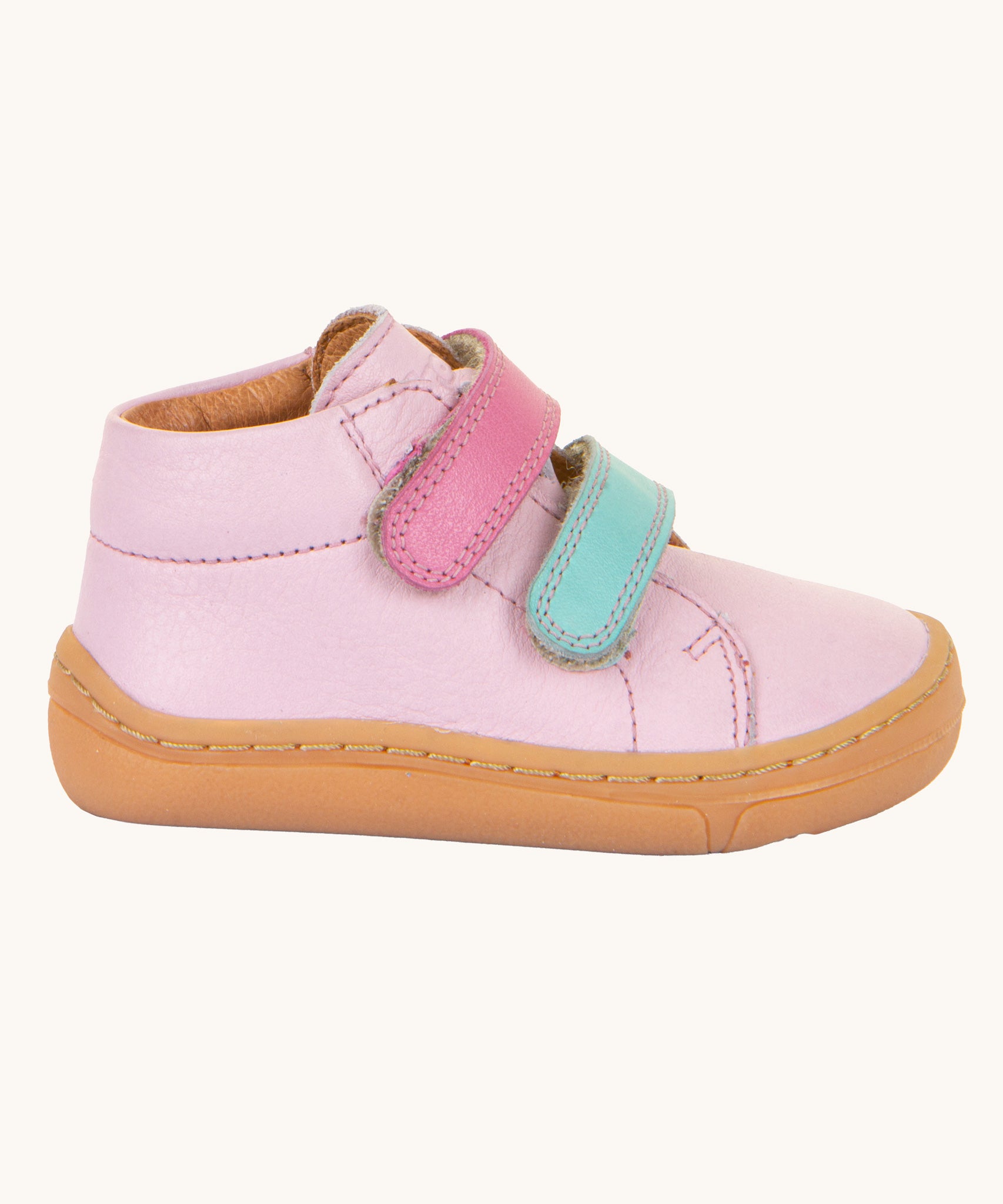 A view of the side profile of the Froddo first step shoes in pink available at Babipur. A soft ankle high natural leather shoe in light pink with 2 velcro straps on the front in dark pink and light blue. Features a light brown rubber grippy sole and a padded ankle support.