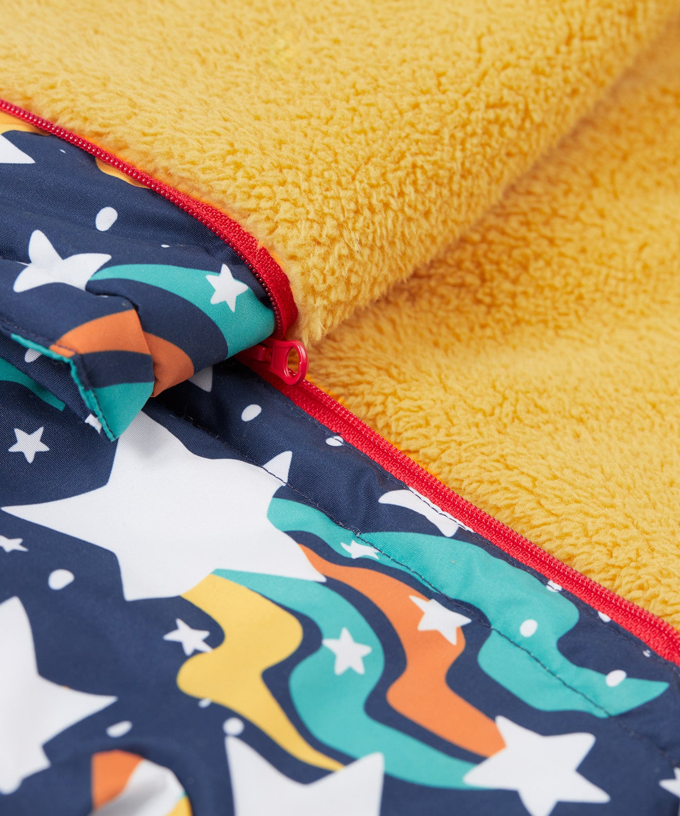 A close up of the Frugi 2 in 1 rambler coat and trousers in magic stars. Showing the yellow fleece inner liner and red zip detail separating the coat and trouser