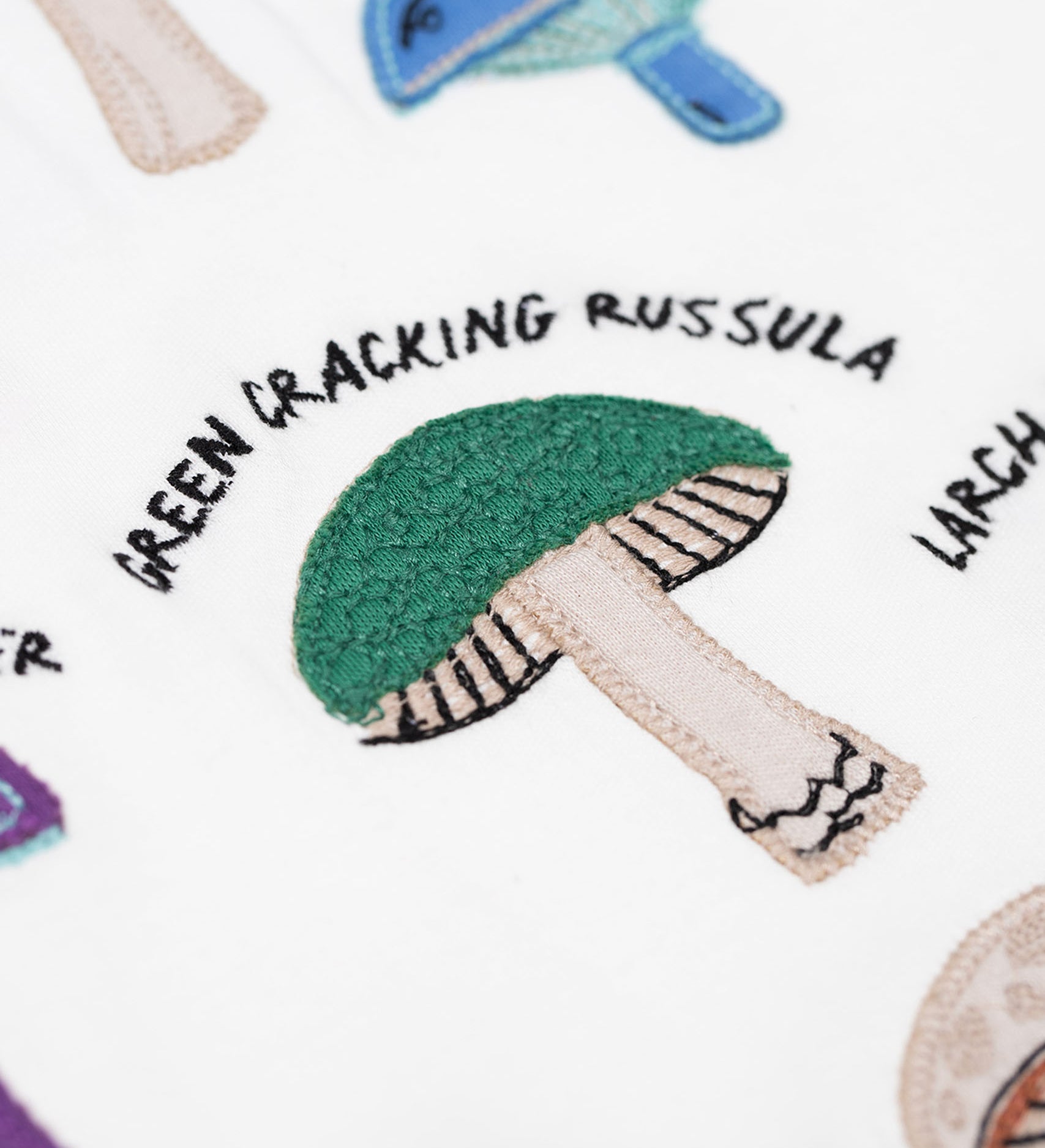 A close up of the green cracking russula fungi on the Frugi Children's Organic Ace Applique Top - White / Mushrooms.