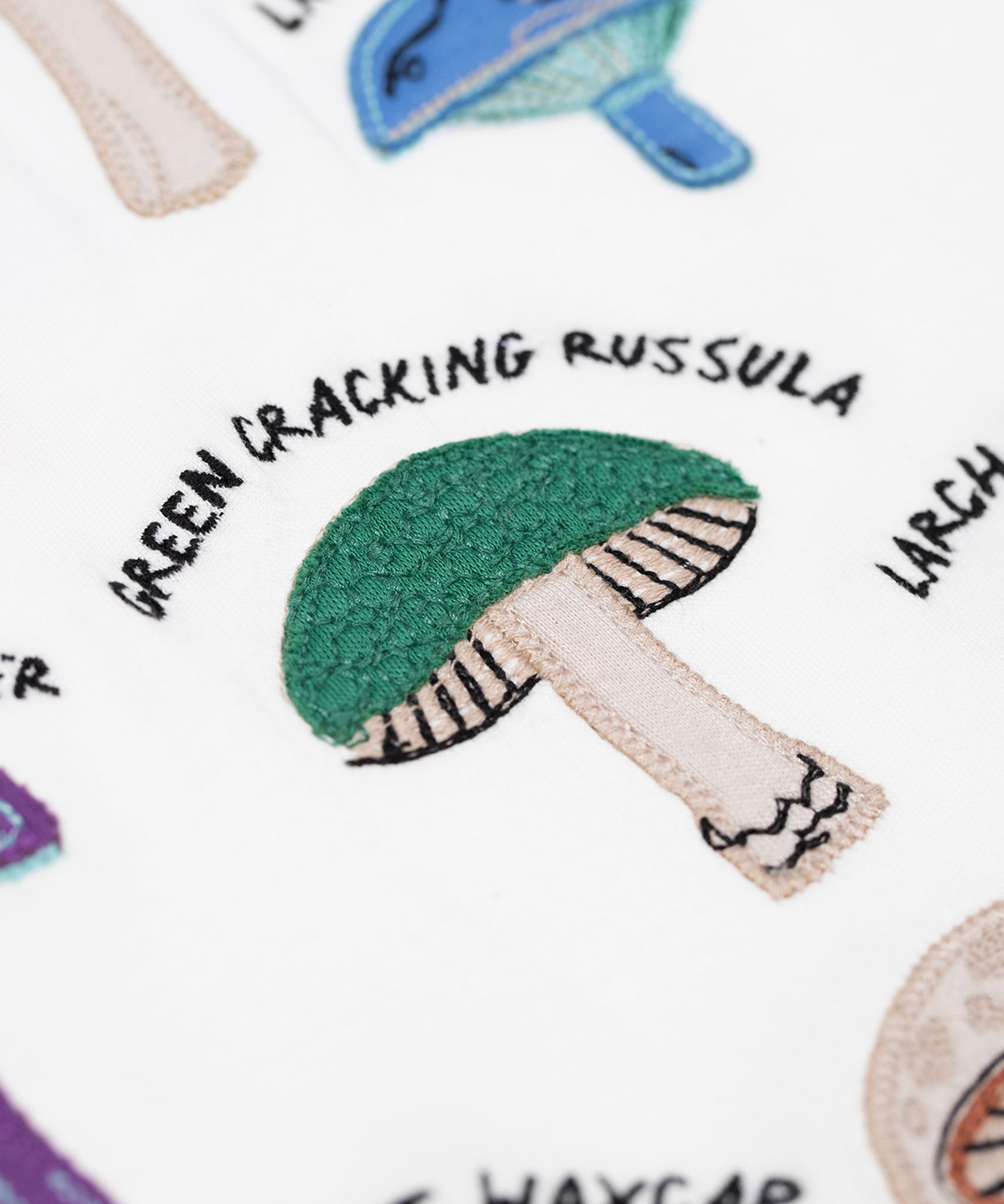A close up of the green cracking russula fungi on the Frugi Children's Organic Ace Applique Top - White / Mushrooms.