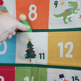 Close up of a green Grapat Nin wooden peg doll being placed into one of the pockets on the Frugi forest festive fun organic cotton advent calendar.