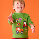 Child wearing the Frugi adventure applique organic cotton long sleeved kids' top in a palm green with tractor appliques on the front.