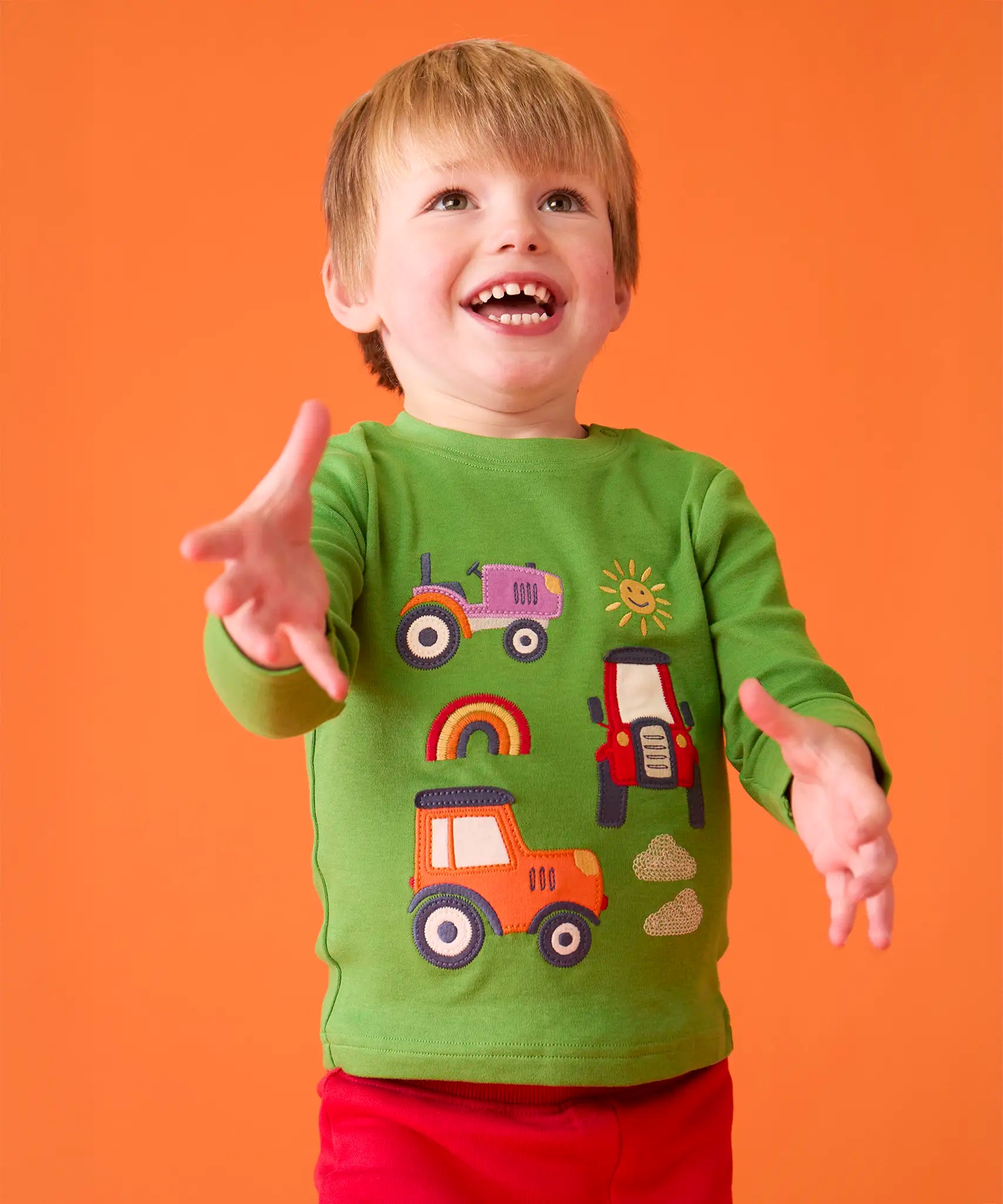 Child wearing the Frugi adventure applique organic cotton long sleeved kids' top in a palm green with tractor appliques on the front.