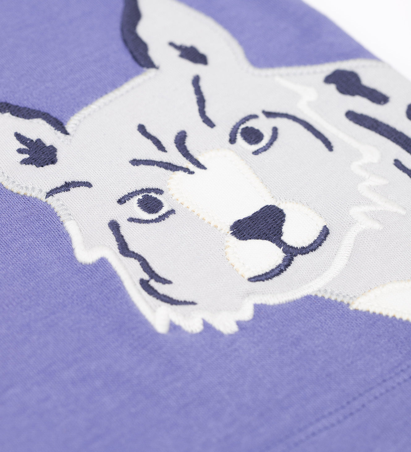 A close up of the snow leopard applique on the Frugi Adventure big cats Applique organic cotton long sleeved top. This top features three big cat appliques on a grape purple coloured background. This top is a part of a wide range of organic cotton clothing for children available here at Babipur. 