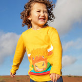 Child wearing the Frugi adventure circular cotton top in bumblebee yellow with a Highland cow applique on the front and denim jeans.