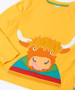 Close up of the Frugi adventure circular cotton top in bumblebee yellow with a Highland cow applique on the front.