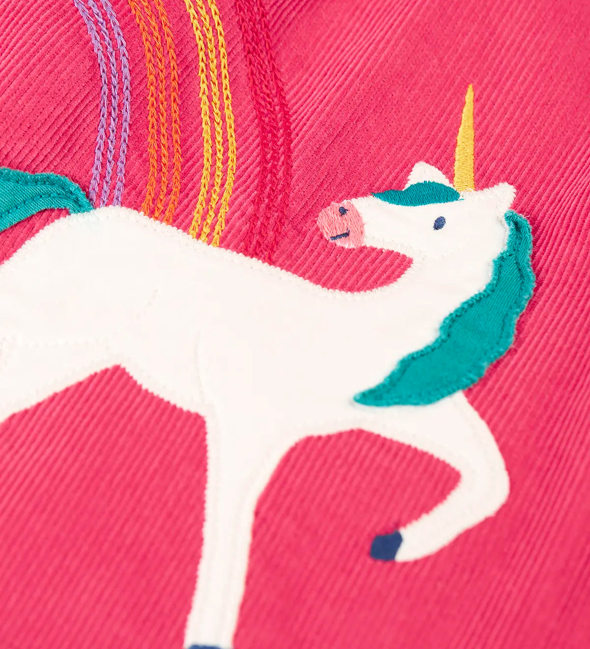 Close up of the unicorn applique and embroidered rainbow detail on the Frugi agatha organic cotton pink corduroy pinafore child's dress.