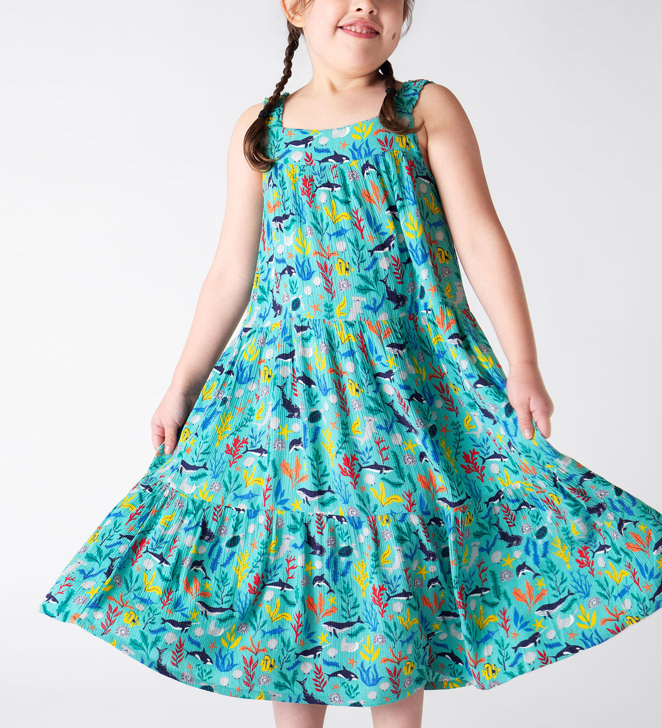 A smiling young child wearing the Frugi Alani Midi Dress featuring a Sea Life print, twirling the dress around.