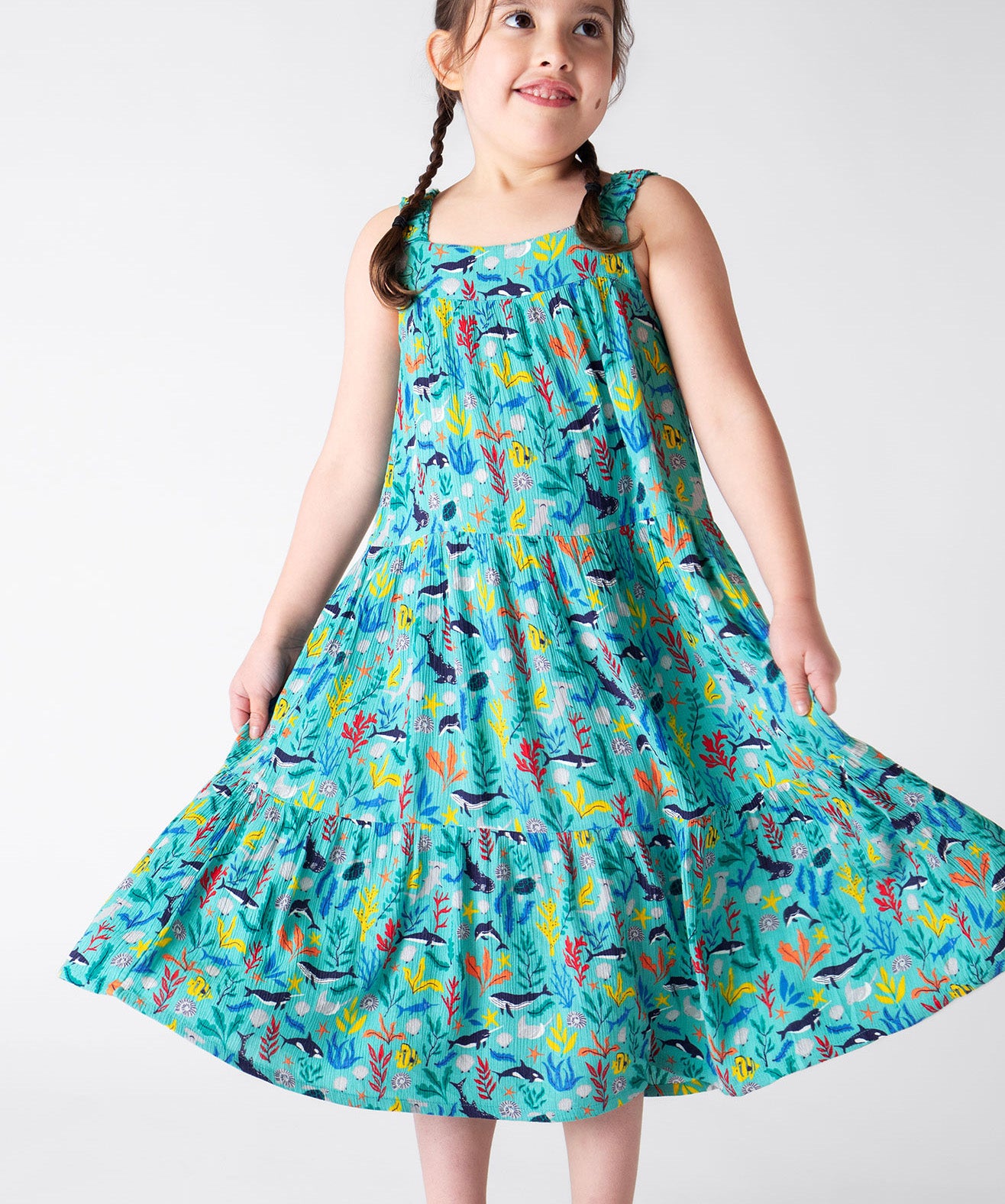 A smiling young child wearing the Frugi Alani Midi Dress featuring a Sea Life print, twirling the dress around.