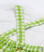 Close up of the Frugi kids Alfred dungarees outfit showing the white sleeve t-shirt and green gingham shoulder straps of the dungaree on organic cotton fabric