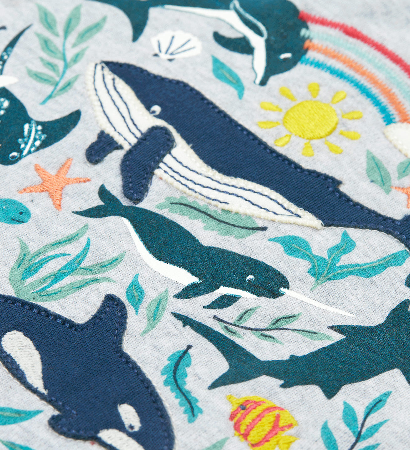 A close up of Frugi Alice Applique T-Shirt in Grey Marl's Sea Life print, featuring embroidered dolphins, whales and smaller fish.