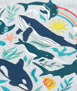 A close up of Frugi Alice Applique T-Shirt in Grey Marl's Sea Life print, featuring embroidered dolphins, whales and smaller fish.