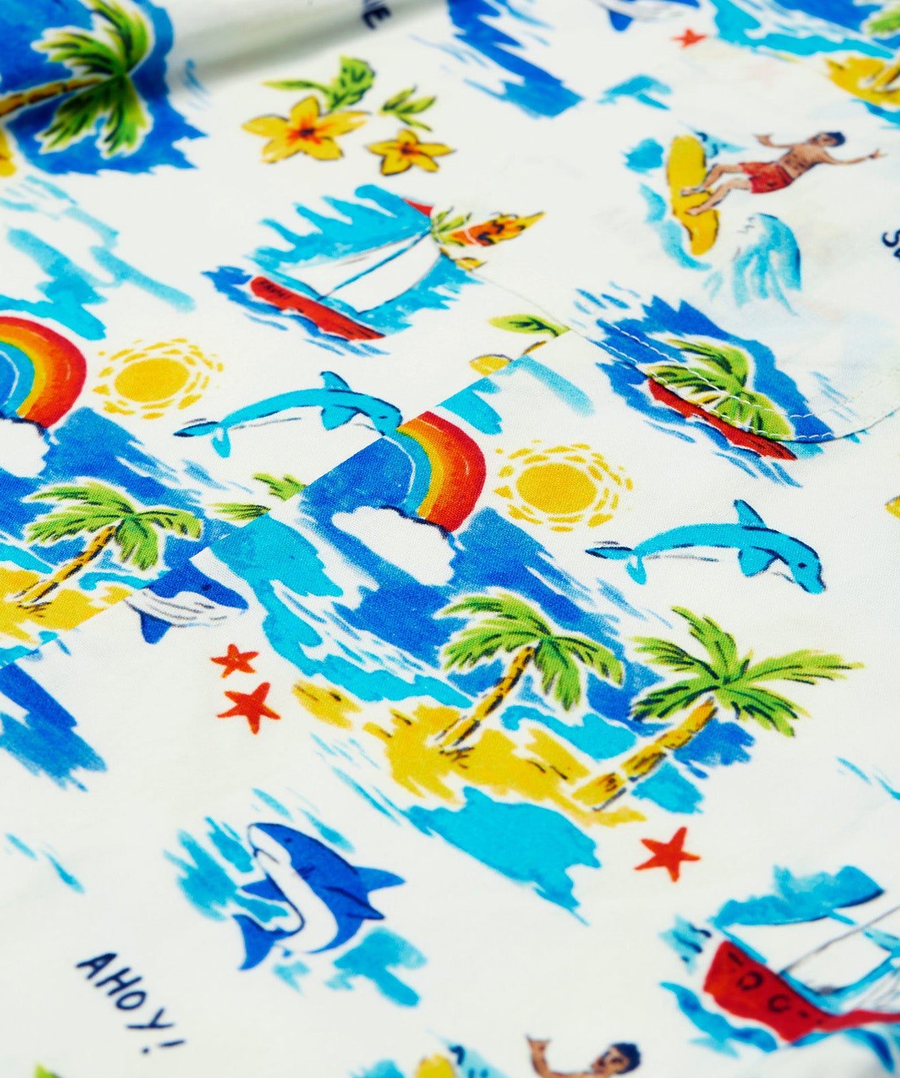 Close-up of the Frugi Aloha Organic Cotton Dungarees, featuring a colourful tropical beach print with dolphins, rainbows and sailing boats.
