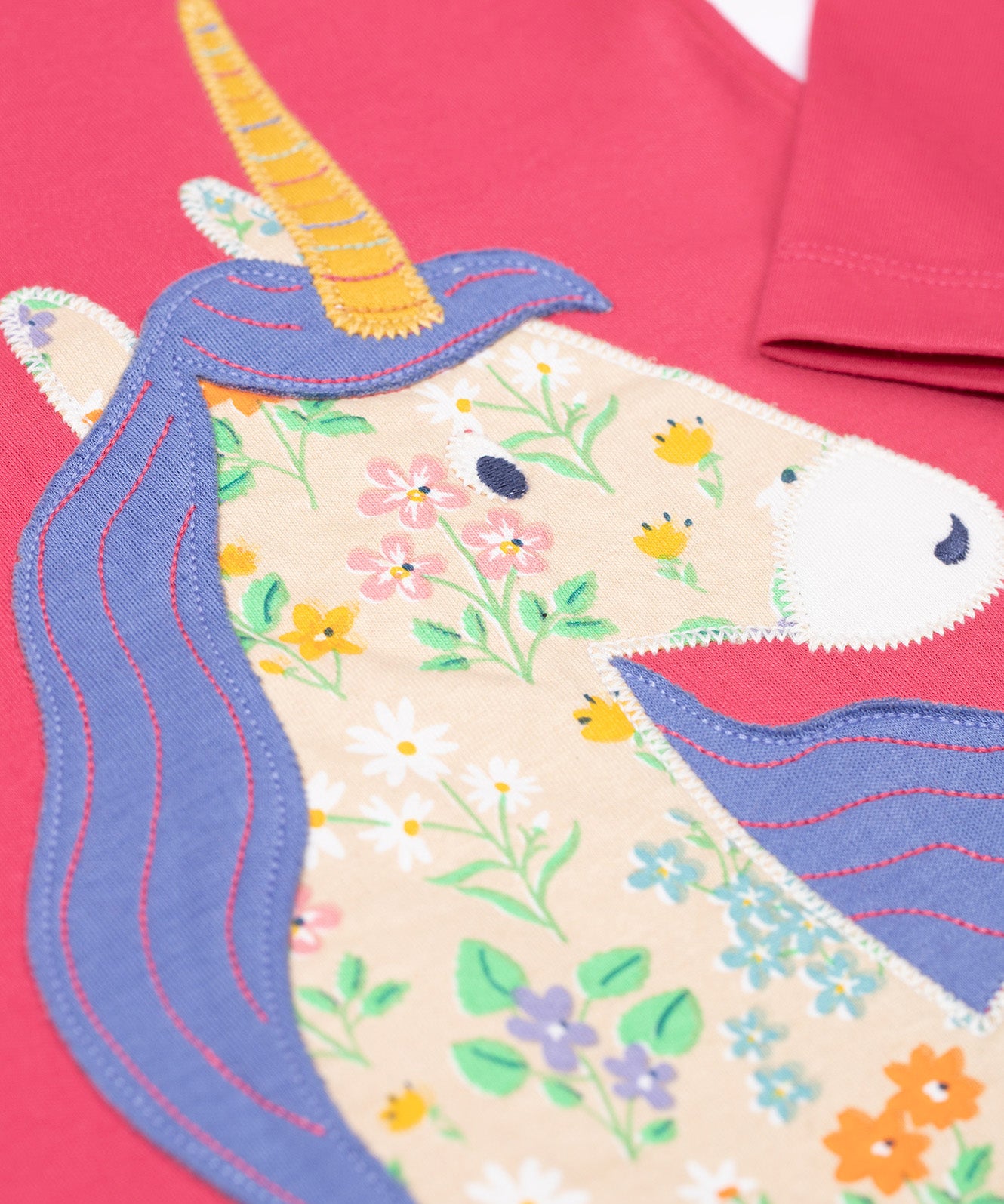 A super close up of teh unicorn applique on the front of the Frugi Rose Pink  Unicorn Anna Circular Organic Cotton Top. A pink coloured long sleeved top with a floral print unicorn applique on the front. This top is a part of a wide range of organic cotton clothing for children available here at Babipur. 