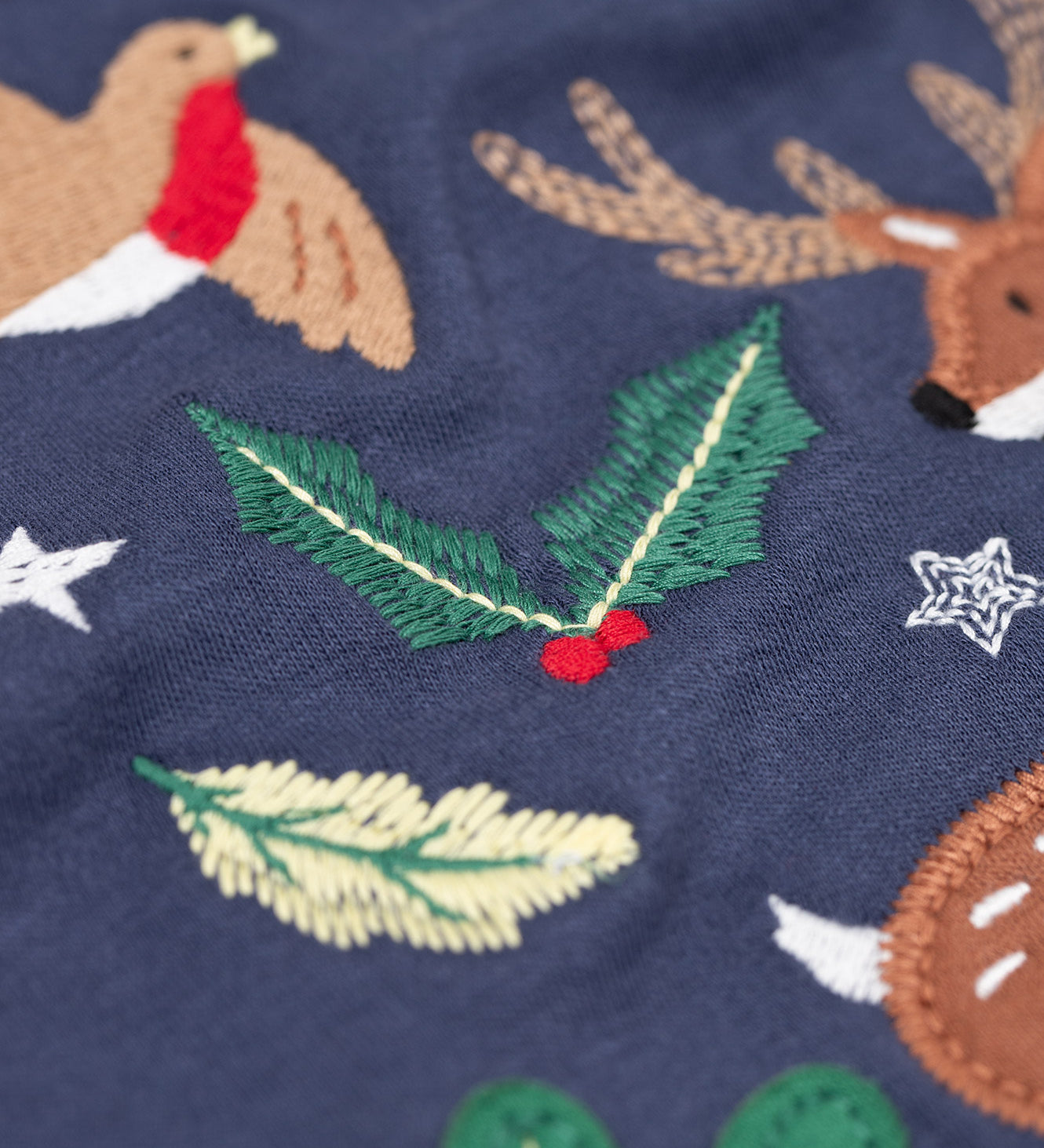 A close up of the embroidered holly detail on the front of the Frugi navy reindeer applique  Organic Cotton Anna long sleeved Top. This top is a part of a wide range of organic cotton clothing for children available here at Babipur.  