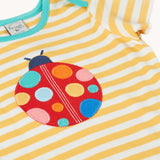 Close up of the front of the Frugi yellow striped short sleeve t-shirt with ladybird applique on the front. The ladybird has rainbow coloured dots.