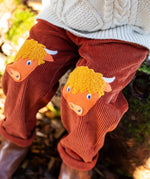 Close up of the highland cow knee patch appliques on the Frugi Arlo rust brown cord trousers, Child wearing with cable knit cream jumper.