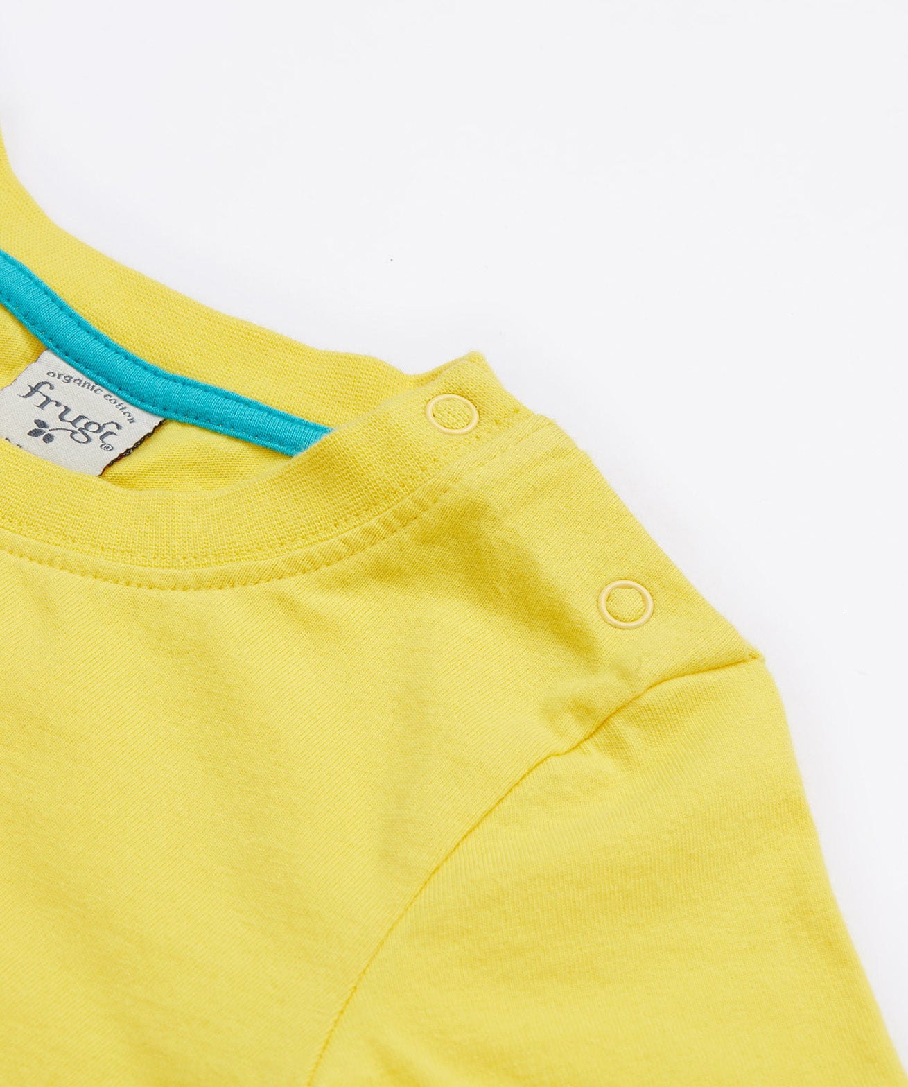 A close up of Frugi Avery Appligue T-Shirt in Welly Yellow, featuring a popper fastenings.