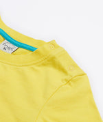 A close up of Frugi Avery Appligue T-Shirt in Welly Yellow, featuring a popper fastenings.