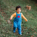 A child running on grass wearing the blue Frugi Babipur cord dungarees. 