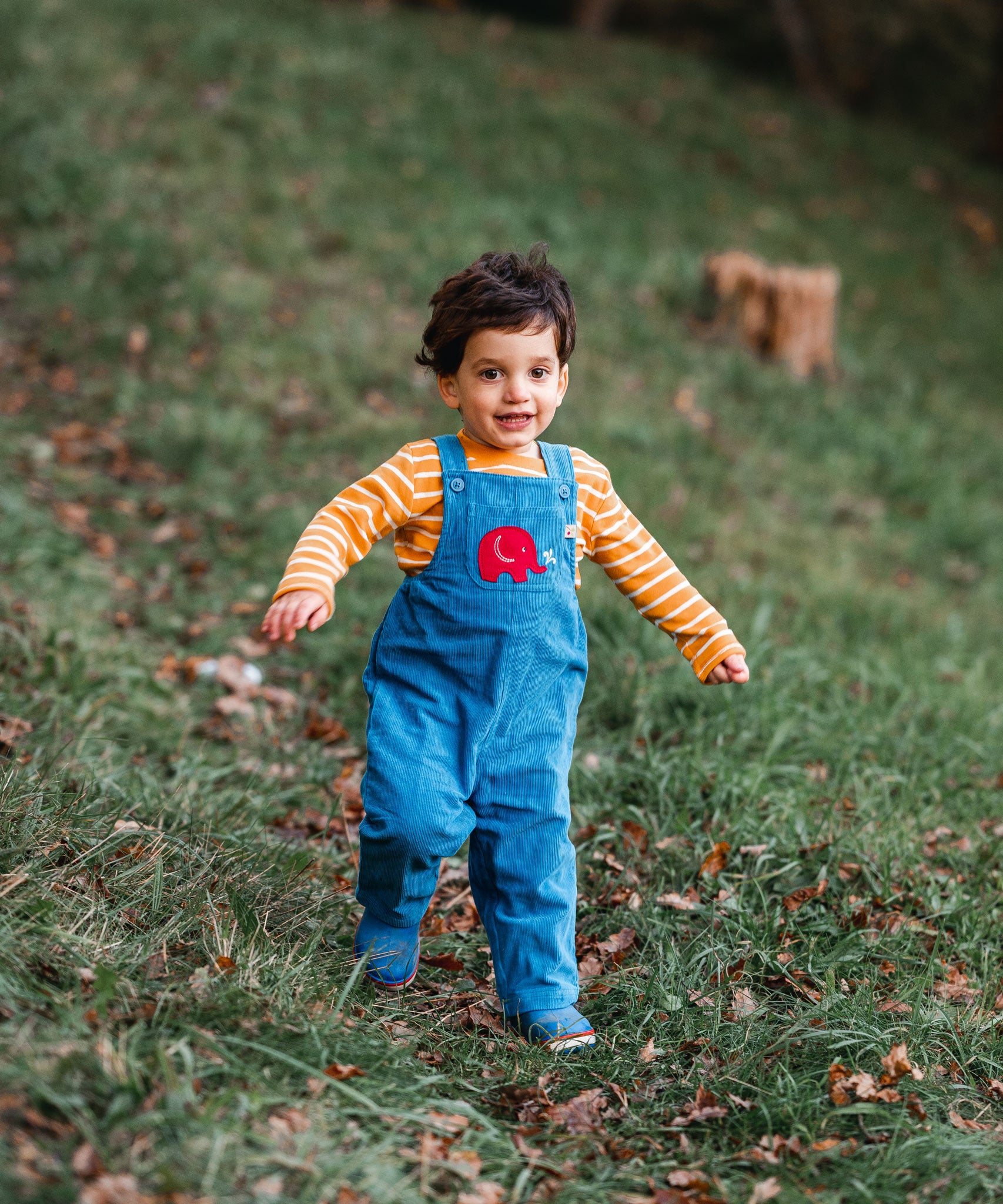 A child running on grass wearing the blue Frugi Babipur cord dungarees. 