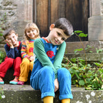 A child sitting on  steps outdoors wearing the blue Frugi Babipur cord dungarees. 