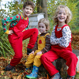 Three children sitting on a large tree stump. Two are wearing the red Frugi Babipur cord dungarees and one is wearing teh yellow version. 