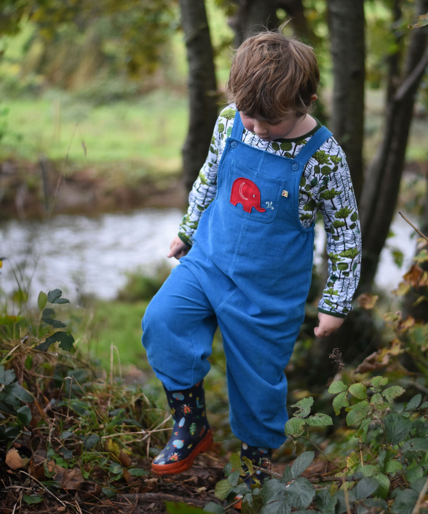 A child walking near a river wearing the blue Frugi Babipur cord dungarees. 