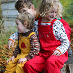 Three children sitting on a large tree stump. All of them are wearing Frugi Babipur cord dungarees. 
