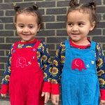 Twins wearing the Frugi Babipur dungarees, one in red, one in blue. 