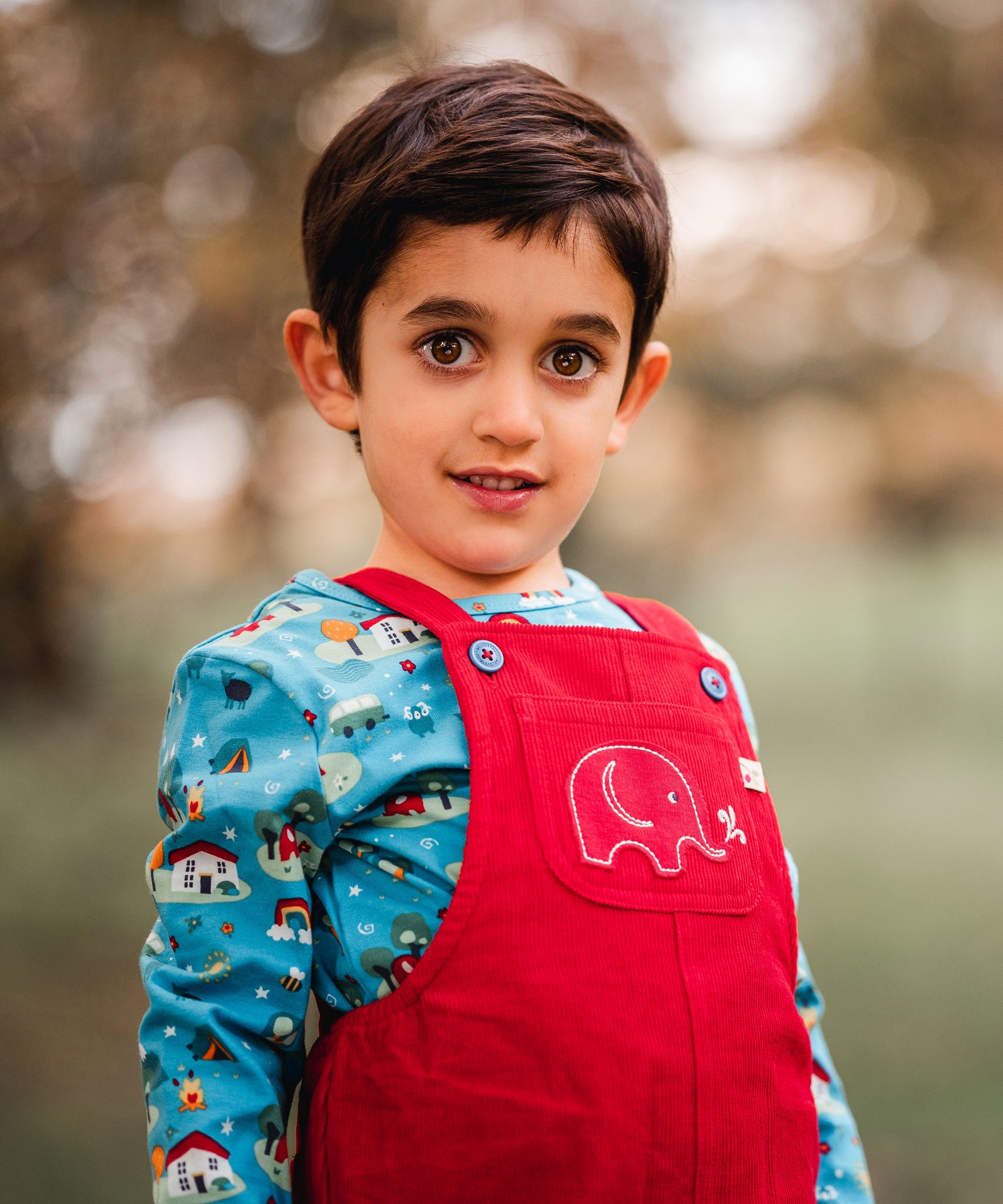 A child wearing teh red cord Frugi Babipur Dungarees showing a close up of the elephant applique detail on the front pocket. The child is wearing the Frugi Dan Y ser top underneath. 