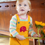 A toddler wearing the yellow cord Frugi Babipur dungarees holding onto large sunflowers. 