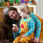 A child wearing the Frugi Babipur yellow cord dungarees, playing with wooden toy figures with his mother.