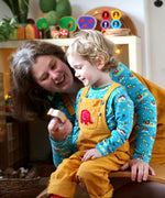A child wearing the Frugi Babipur yellow cord dungarees, playing with wooden toy figures with his mother.