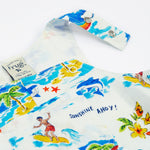A close-up of the Frugi Aloha Organic Cotton Dungarees front pocket and popper fastenings, featuring a colourful tropical beach print with dolphins, rainbows and sailing boats.