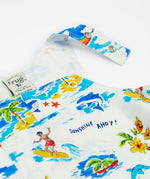 A close-up of the Frugi Aloha Organic Cotton Dungarees front pocket and popper fastenings, featuring a colourful tropical beach print with dolphins, rainbows and sailing boats.