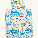 Frugi Aloha Organic Cotton Dungarees laid flat, showing a vibrant all-over tropical print with sailing ships, dolphins, rainbows, palm trees, surfers, and beach motifs on a white background, featuring front pocket and popper fastenings.