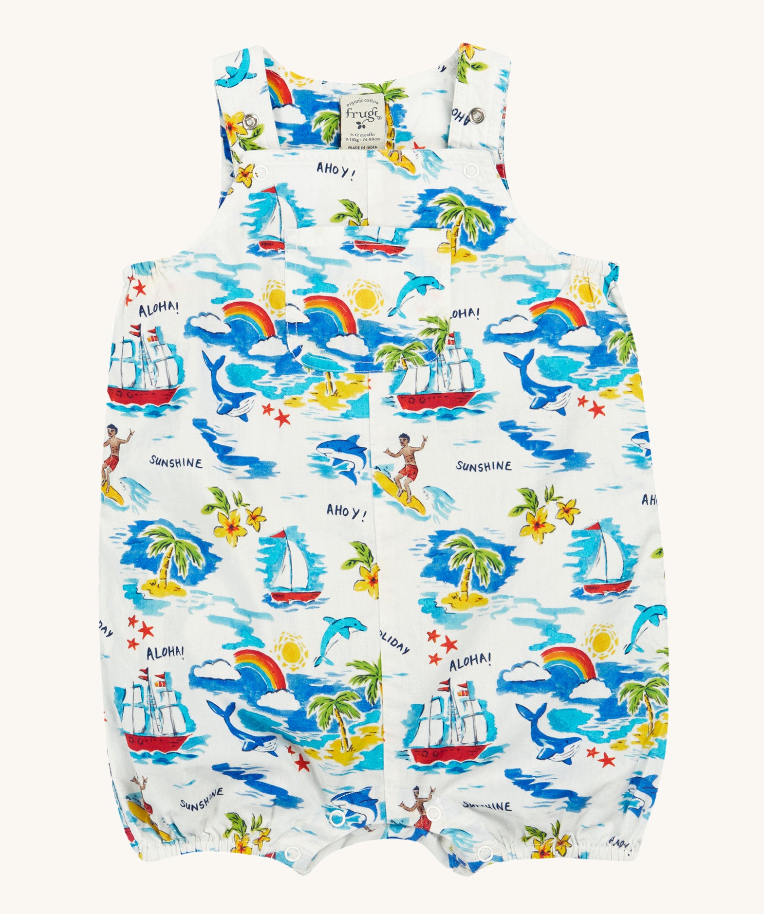 Frugi Aloha Organic Cotton Dungarees laid flat, showing a vibrant all-over tropical print with sailing ships, dolphins, rainbows, palm trees, surfers, and beach motifs on a white background, featuring front pocket and popper fastenings.