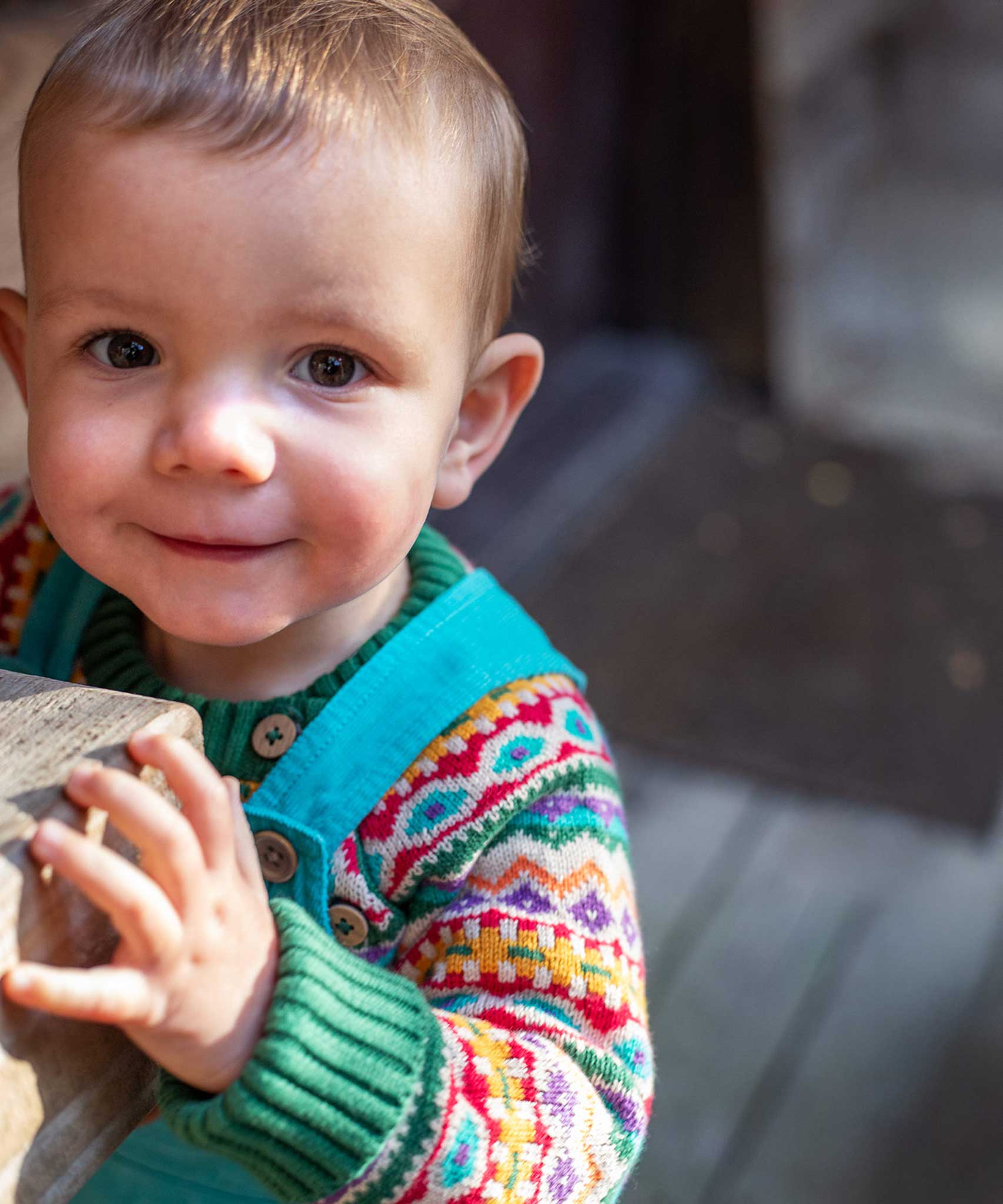 A child wearing the Frugi fowey bear fairisle organic cotton knitted jumper. underneath a blue coloured cord dungarees. 