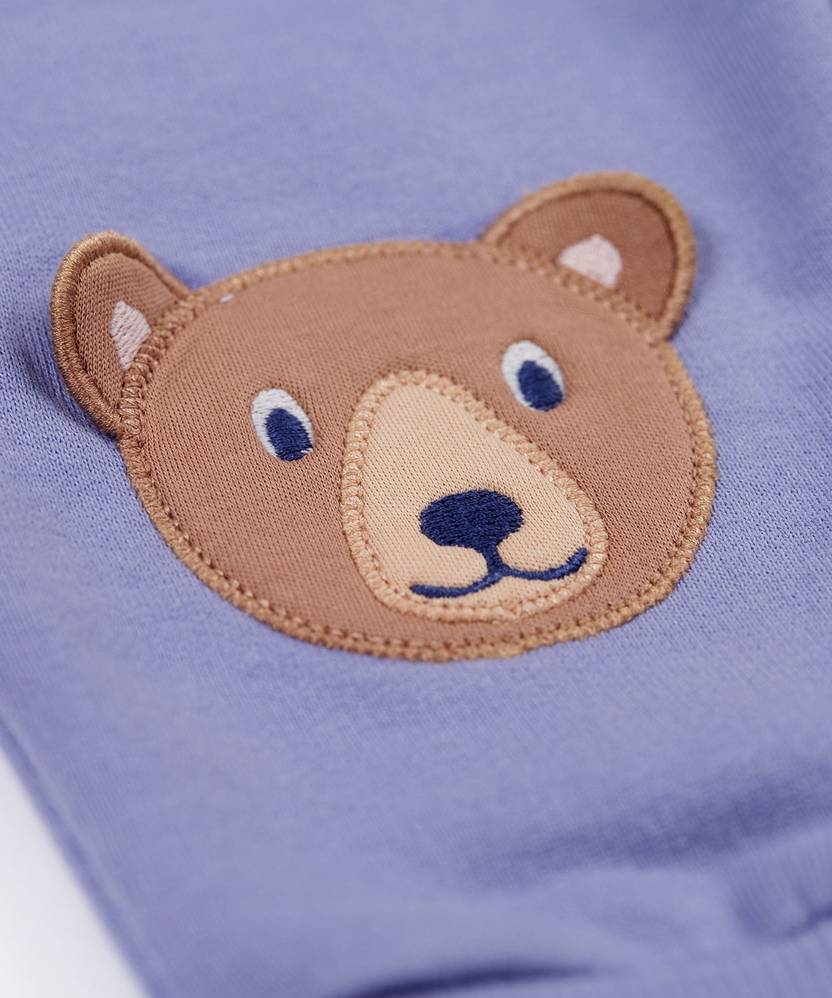 A close up of the brown bear applique on the knees of the Frugi bear character grape purple coloured children's crawlers.