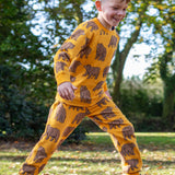 A child running outside and wearing the Frugi beary wild parsnip joggers. A dark yellow GOTS organic joggers with a brown bear print. 