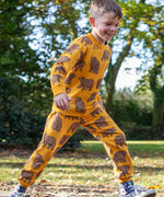 A child running outside and wearing the Frugi beary wild parsnip joggers. A dark yellow GOTS organic joggers with a brown bear print. 