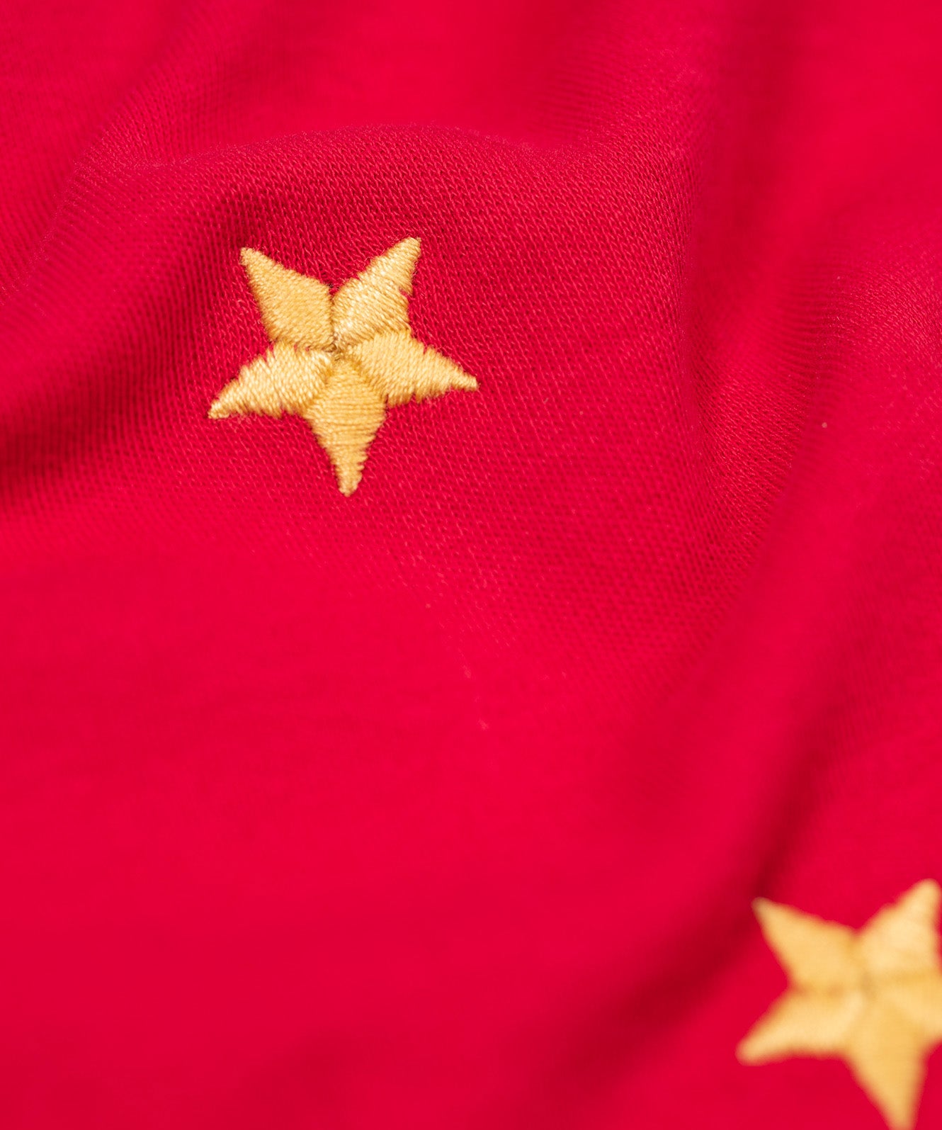 A close up of the gold embroidered star detail on the front of the Frugi Berry Red Reindeer Terrific Circular Organic Cotton long sleeved kids Top. A red coloured children's top with a festive reindeer applique and gold stars on the front. This top is a part of a wide range of organic cotton clothing for children available here at Babipur. 