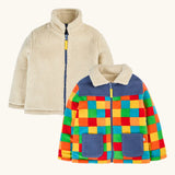 both sides of the frugi fleece jacket, one side in solid cream and one in a bright multicolor patchwork pattern with blue panels and pockets.
